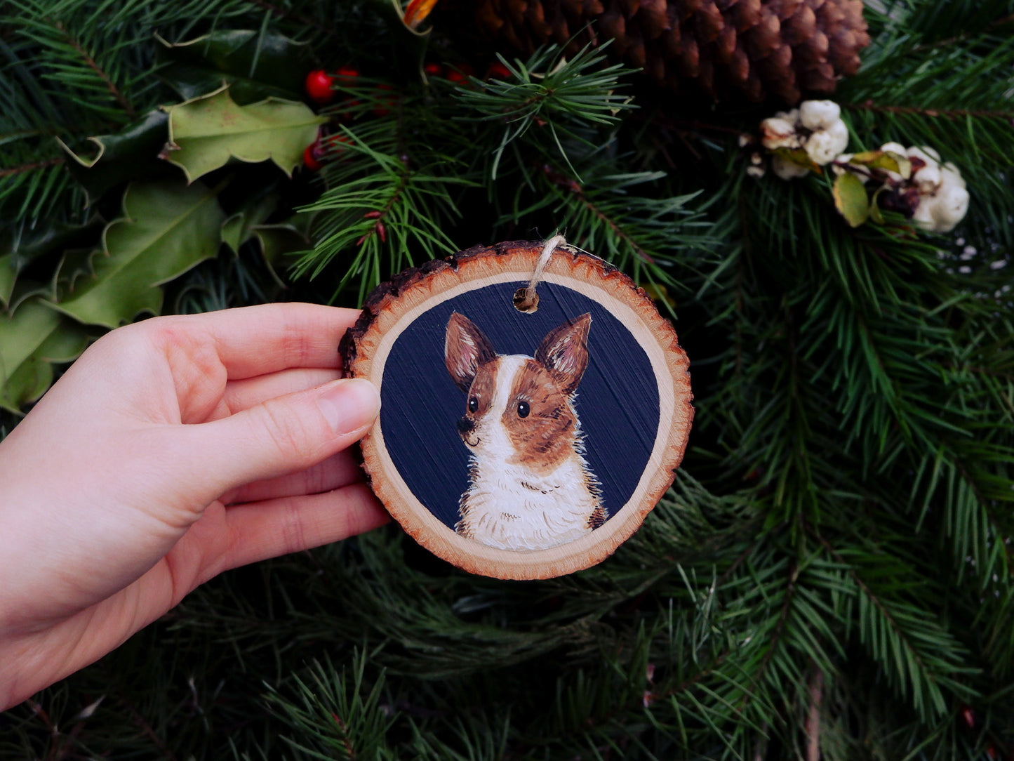 Hand holding a wooden ornament with a dog illustration against a green leafy background