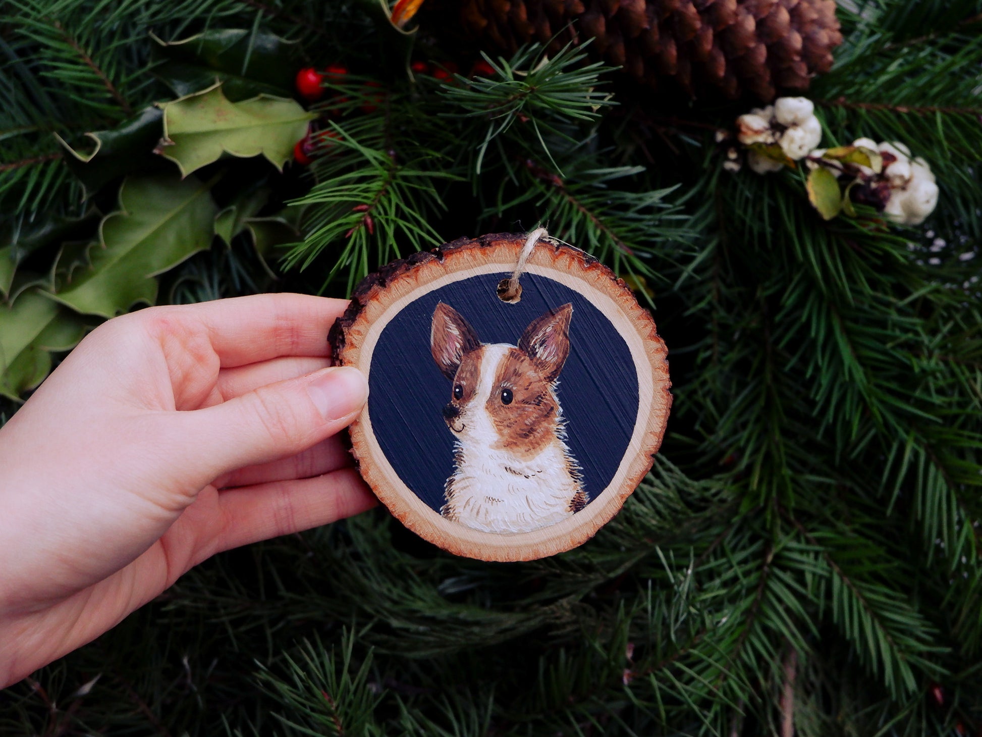 Hand holding a wooden ornament with a dog illustration against a green leafy background